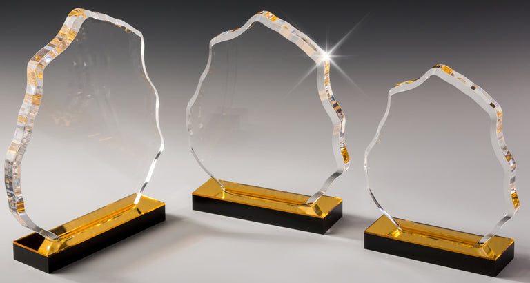 Drei klare, einzigartig geformte Awards Leverkusen 3-er Serie (178x178 mm - 229x203 mm ) mit goldenen und schwarzen Sockeln sind auf grauem Hintergrund abgebildet, wobei einer glitzert, um die komplizierten Lasergravur-Details zu betonen.