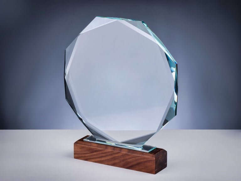 Eine klare, achteckige Glastrophäe mit aufwendiger Lasergravur auf Holzsockel, auf weißer Fläche vor grauem Hintergrund. Awards Frankfurt am Main 200x40x230 mm von POMEKI.
