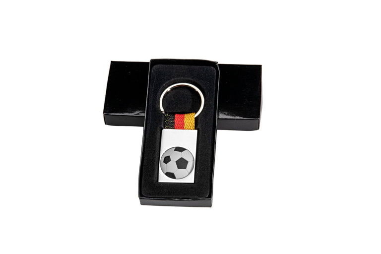 Ein Schlüsselanhänger Fussball mit einem Riemen in Schwarz, Rot und Gelb, verpackt in einer schwarzen rechteckigen Box.