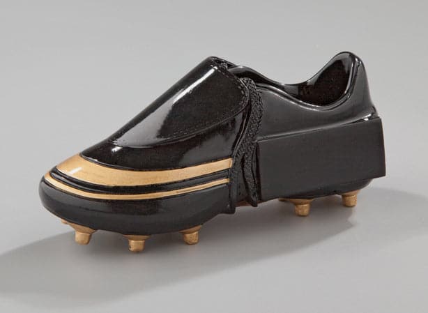 Ein schwarzer Schuh mit goldenen Akzenten, mit dickem Absatz und Nieten wie bei einem Fußballschuh, vor einem neutralen Hintergrund. Dieses aus hochwertigem Material gefertigte Einzelstück ist ein echter Trophäe-Fußballschuh 130x55 mm und sticht in jeder Sammlung hervor.