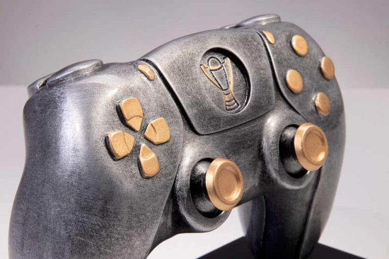 Nahaufnahme eines metallischen Trophäen-Controllers 150 mm x 188 mm, gefertigt aus hochwertigem Material mit goldenen Knöpfen und Details, mit einem exklusiven Design und einem Trophäen-Emblem in der Mitte.