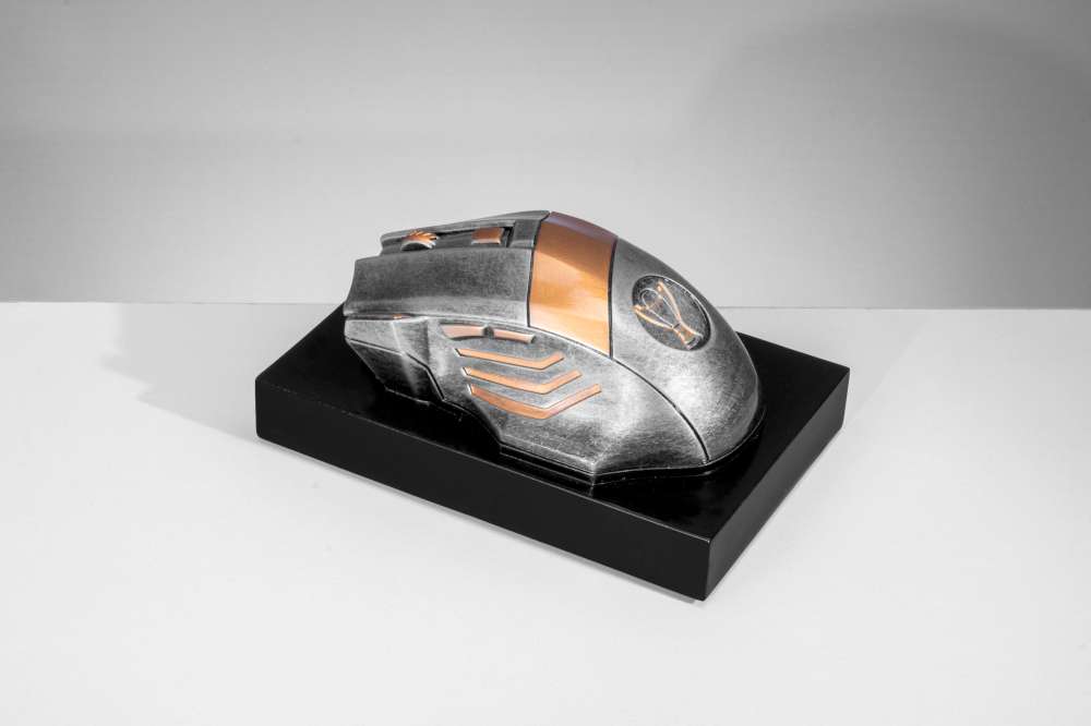 Eine metallische Computermaus mit futuristischem Design, Kupferakzenten und einem Logo sitzt auf einem schwarzen rechteckigen Ständer unter neutraler Beleuchtung und ähnelt einer eleganten Trophäe Computer Maus 70 mm x 150 mm PK739678-62593-E25.