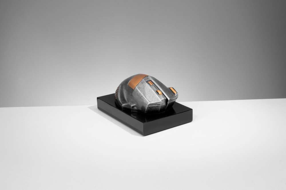 Eine kleine, futuristische Skulptur mit geometrischen Formen, überwiegend in Grau mit bronzenen Akzenten, präsentiert auf einem rechteckigen schwarzen Sockel – eine perfekte Trophäe Computer Maus 70 mm x 150 mm PK739678-62593-E25.