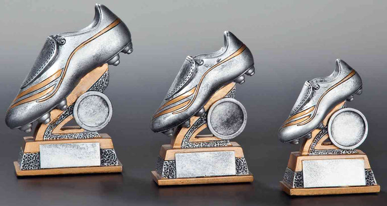Drei Fußballschuh-Trophäen der 3er-Serie Fußball mit silbernem Design und goldenen Details an den Schuhen, auf quadratischen Sockeln mit Platz für Inschriften, in absteigender Größe (104 mm bis 142 mm). Von POMEKI.