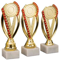 Thumbnail for Drei goldene Pokale Hilden mit roten Akzenten auf Marmorsockeln.