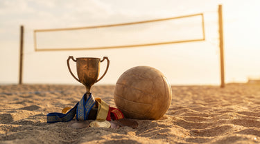 Pokal und Medaillen mit Bändern im Sand neben einem Volleyball am Beachfeld