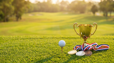 Eleganter Pokal und Medaillen auf dem Grün neben einem Golfball auf dem Tee