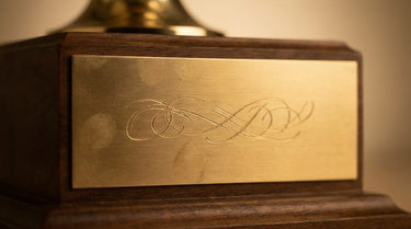Goldene Gravurplakette am Sockel eines Pokals – KI-generiertes Symbolbild