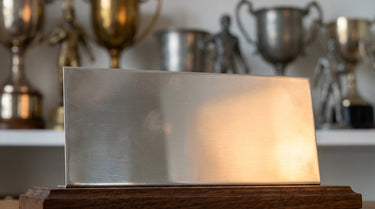 Blanko-Gravurschild an einem Pokal, im Hintergrund weitere Pokale – KI-generiertes Symbolbild