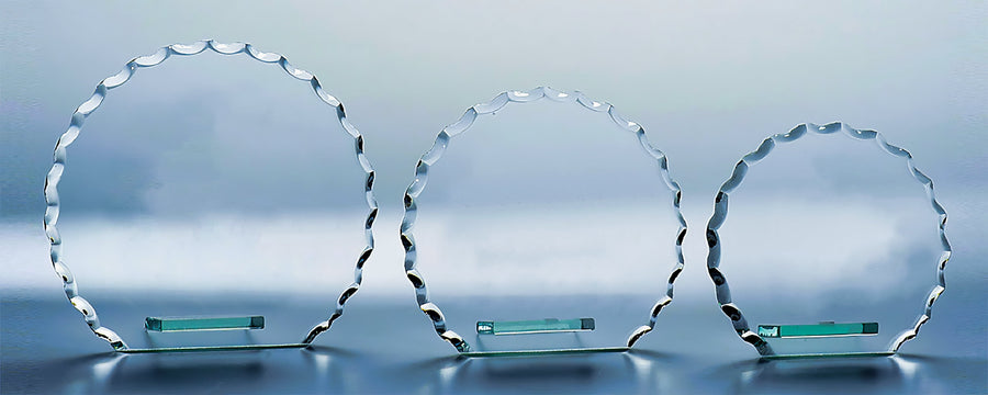 Drei ovale Glastafeln mit gewellten Kanten, die jeweils einem eleganten Glaspokal Leipzig 3-er Serie 105 mm – 145 mm PK735213-11-3-E50 ähneln, stehen stolz auf kleinen grünen rechteckigen Sockeln vor einem grauen Hintergrund.