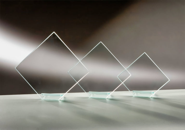 Drei transparente, rautenförmige Glasauszeichnungen mit Lasergravur auf hellgrauer Oberfläche vor dunklem Hintergrund mit Farbverlauf. Awards Bonn 3-er Serie 120x140 mm – 178x200 mm von POMEKI.