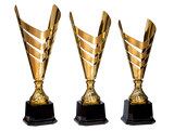 Drei goldfarbene Trophäen mit schwarzem Sockel sind in einer Reihe vor einem grauen Hintergrund ausgestellt. Die Trophäen (Pokale Bünde 3-er Pokalserie 427 mm - 497 mm ) haben ein modernes, offenes Design mit abgewinkelten, überlappenden Abschnitten.