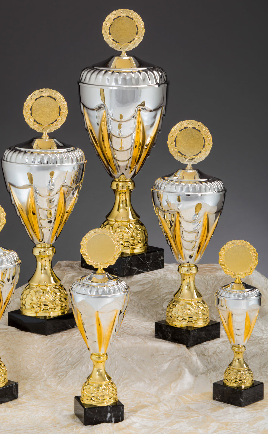 Eine Sammlung von Gold- und Silbertrophäen mit schwarzem Sockel, in verschiedenen Größen, präsentiert auf einer leicht strukturierten Oberfläche. Diese Pokale Nordhausen 5-er Pokalserie 275 mm - 444 mm PK757910-5-E50 sind aus hochwertigem Material gefertigt und zeichnen sich durch ein exklusives Design aus, das hervorsticht.