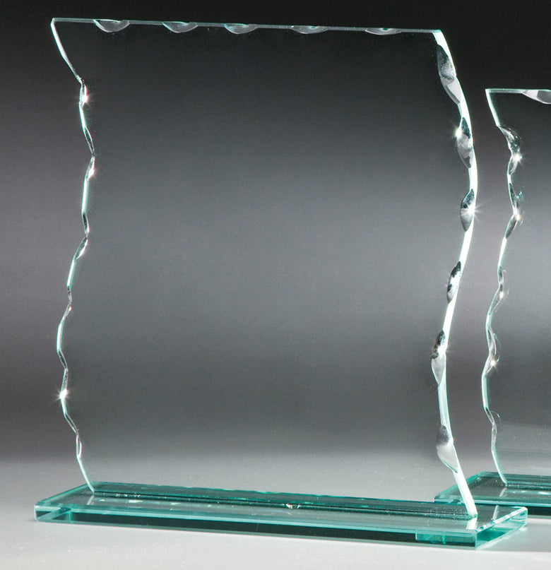 Der Glaspokal Hannover 3-er Serie 105x135 mm – 200x190 mm PK766623-21-3-E50 ist eine klare, rechteckige Glasauszeichnung mit gewellten Kanten und einer asymmetrischen Oberseite, montiert auf einem Glassockel und mit einem komplizierten Gravurschild-Emblem vor einem dunkelgrauen Hintergrund versehen.