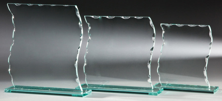 Drei Auszeichnungen der Glaspokal Hannover 3-er Serie in unterschiedlichen Größen, jede mit gezackten Oberkanten und auf rechteckigen Glassockeln montiert, stehen stolz vor einem neutralen Hintergrund. Die größte Trophäe mit den Maßen 200 x 190 mm trägt das INKLUSIVE-Emblem und steht für Präzision und Eleganz.