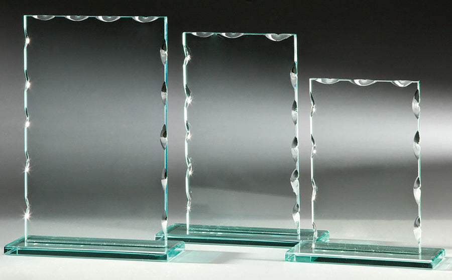 Drei rechteckige Auszeichnungen aus klarem Glas, Awards Karlsruhe 3-er Serie 150x120 mm – 198x150 mm PK766633-31-3, mit dekorativen, geschwungenen Kanten mit präziser Lasergravur, sind nebeneinander auf einem grauen Hintergrund angeordnet.
