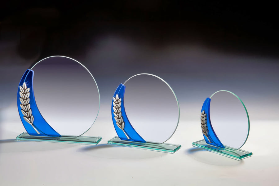 Drei runde Glastrophäen in unterschiedlichen Größen, jede mit einem blauen Akzent und einem silbernen Lorbeerdesign auf einem Farbverlaufshintergrund. Diese Awards Bremen 3-er Serie 121 mm - 185 mm PK767198-96-3 sind der Inbegriff von Komfort und Design und zeigen Eleganz durch aufwendige Lasergravur.