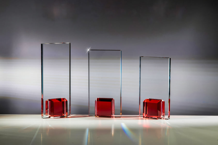 Drei rechteckige Glaspokal-Essen-Auszeichnungen aus der 3er-Serie, jeweils mit rotem Sockel und wunderschön eingraviertem Gravurschild, werden auf einer Fläche vor grauem Hintergrund präsentiert.