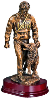 Trophäe Hundeführer 290 mm: Bronzestatue eines Mannes in einem nummerierten Trikot, der neben einem Hund läuft, beide auf einem dunklen Holzsockel. Der Mann blickt auf den Hund herab, der zu ihm aufschaut.
