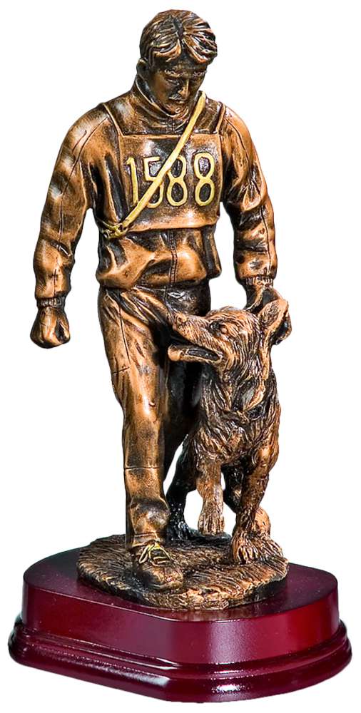 Trophäe Hundeführer 290 mm: Bronzestatue eines Mannes in einem nummerierten Trikot, der neben einem Hund läuft, beide auf einem dunklen Holzsockel. Der Mann blickt auf den Hund herab, der zu ihm aufschaut.