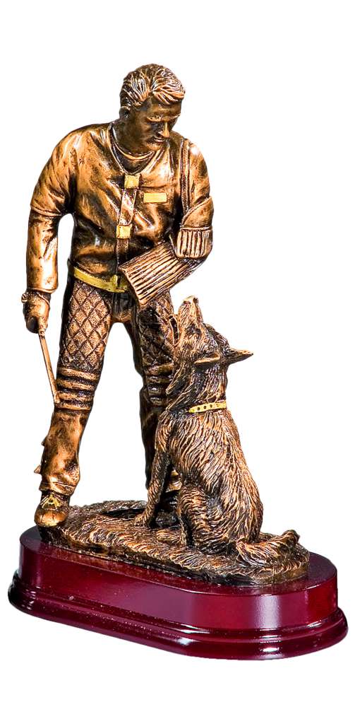 Bronzefarbene Figur eines Mannes mit Schutzarm und Stock, daneben ein sitzender Schäferhund, auf einem dunkelroten Sockel. Trophäe Figurant 300 mm von POMEKI.