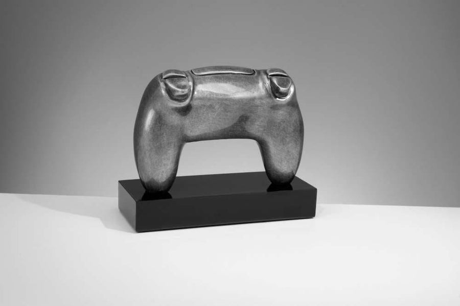 Eine graue Skulptur, die einem Videospiel-Controller ähnelt, aus hochwertigem Material gefertigt, ist auf einem schwarzen rechteckigen Sockel vor einem neutralen Hintergrund montiert. Diese Skulptur ist der Trophäe Controller 150 mm x 188 mm PK739677-62605-E25-G.