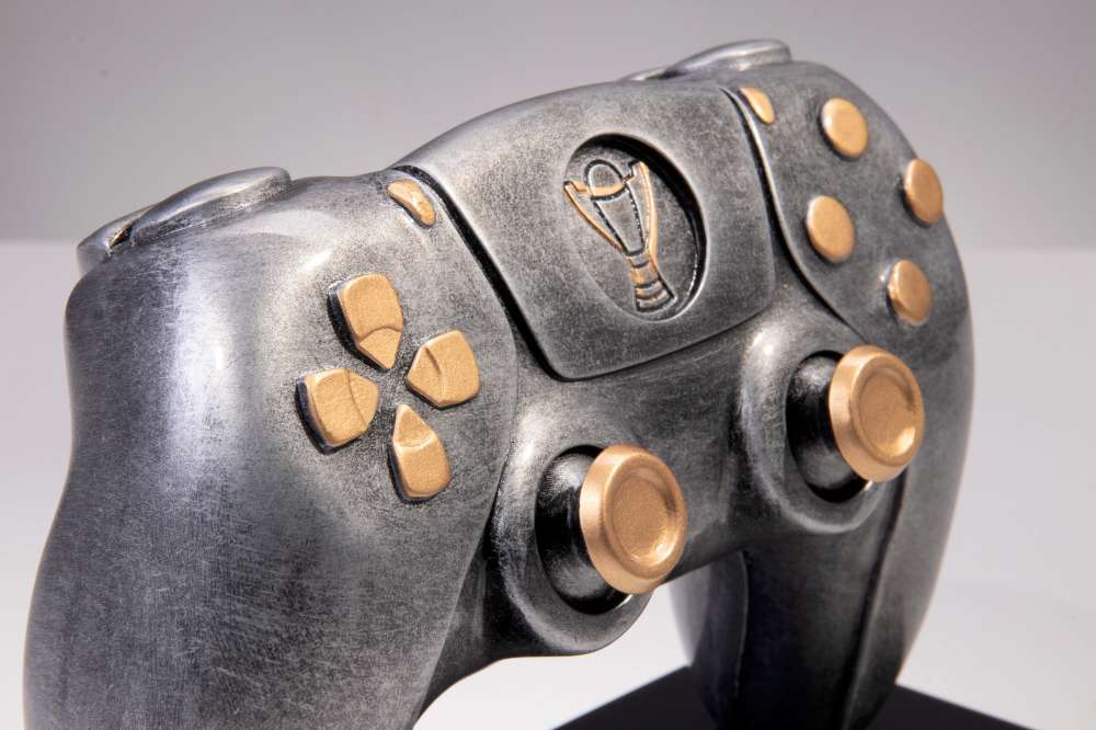 Nahaufnahme eines metallischen Trophäen-Controllers 150 mm x 188 mm PK739677-62605-E25-G, gefertigt aus hochwertigem Material mit goldenen Knöpfen und Details, mit einem exklusiven Design und einem Trophäen-Emblem in der Mitte.
