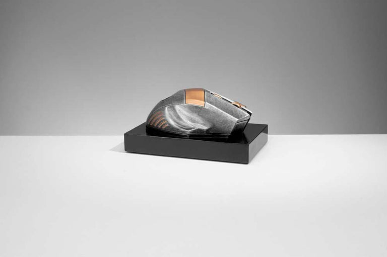 Eine schlanke, metallische Computermaus mit futuristischem Design präsentiert sich als elegante Trophäe Computer Maus 70 mm x 150 mm auf einem schwarzen rechteckigen Ständer vor einem einfachen grauen Hintergrund.