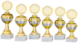 Sechs goldene und silberne Pokale Marburg 6-er Pokalserie 208 mm – 255 mm mit runden Plaketten und Sockeln aus weißem Marmor sind in einer Reihe angeordnet und zeigen ein exklusives Design.