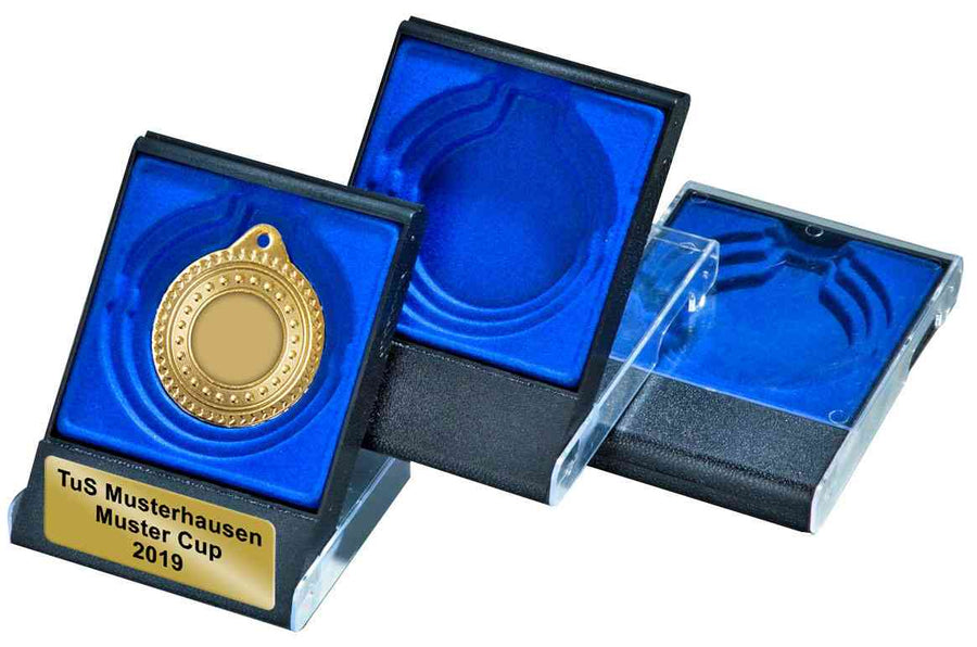Eine Goldmedaille in einem blau-schwarzen Etui für Medaillen inklusive Gravurschild für ⌀ 50-, 60- und 70 mm geeignet PK761849-62593, mit der Aufschrift „TuS Musterhausen Muster Cup 2019.“ Zwei weitere leere Felder sind teilweise geöffnet und warten darauf, von Ihnen mit einem individuellen Wunschtext auf dem Gravurschild versehen zu werden.